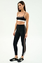 A woman wears the SPLITS59 Layla Airweight High Waist 7/8 in Black/Lentil, paired with a black sports bra and black Adidas sneakers—ideal attire for hot yoga.