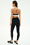 A woman stands facing away in SPLITS59's Layla Airweight High Waist 7/8 leggings in Black/Lentil, featuring side stripes and a cross-back sports bra—ideal for hot yoga—paired with black athletic shoes.