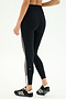 A person wears SPLITS59 Layla Airweight High Waist 7/8 leggings in Black/Lentil with side stripes and black athletic shoes, standing against a plain light background—perfect for hot yoga.