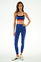A woman poses in a studio wearing the SPLITS59 Scottie Airweight Bra - Cobalt/Indigo with matching high-waisted leggings and white Adidas sneakers.