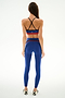 A woman wears the SPLITS59 Emerson Airweight High Waist 7/8 - Cobalt/Indigo, facing away, paired with white shoes with black X markings against a white background.