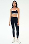 A woman stands against a plain background wearing the SPLITS59 Emerson Airweight Bra in Indigo/Dove Grey, paired with matching high-waisted leggings and white sneakers—perfect for hot yoga sessions.
