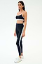 A woman wears the SPLITS59 Emerson Airweight Bra in Indigo/Dove Grey with matching high-waisted leggings, featuring a light blue stripe, styled with white sneakers against a plain light background—ideal for hot yoga.