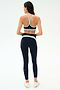 A woman faces away, wearing the SPLITS59 Emerson Airweight Bra in Indigo/Dove Grey with matching high-waisted leggings and white sneakers—ideal for hot yoga—set against a plain background.