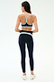 A woman faces away, wearing the SPLITS59 Emerson Airweight Bra in Indigo/Dove Grey with matching high-waisted leggings and white sneakers—ideal for hot yoga—set against a plain background.