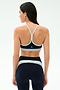 A woman faces away, wearing the SPLITS59 Emerson Airweight Bra in Indigo/Dove Grey with matching high-waisted leggings—ideal for hot yoga—set against a plain, light background.