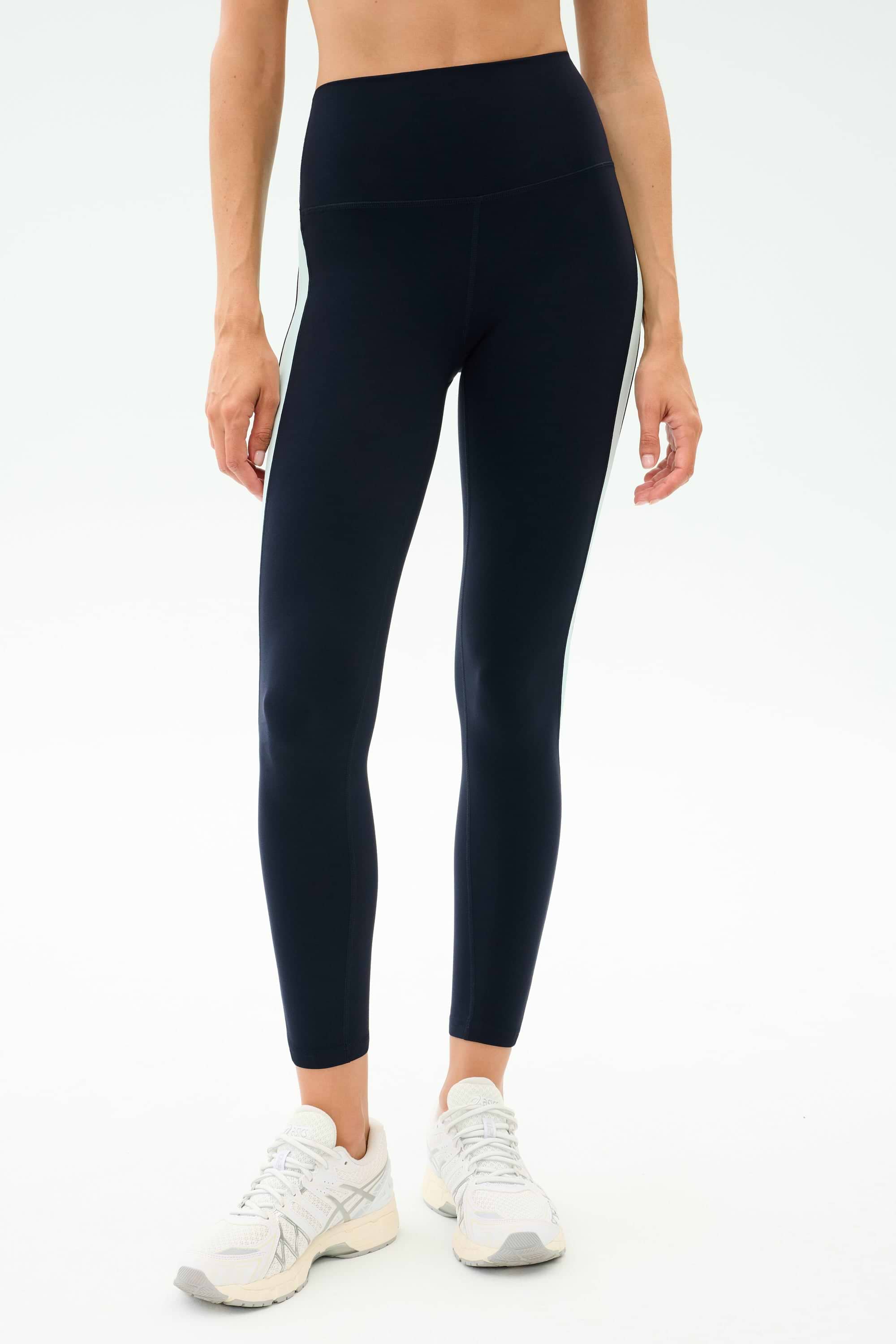 Person wearing SPLITS59 Emerson Airweight High Waist leggings in Indigo/Dove Grey and white sneakers, standing against a plain light background—ideal for Pilates or hot yoga sessions.
