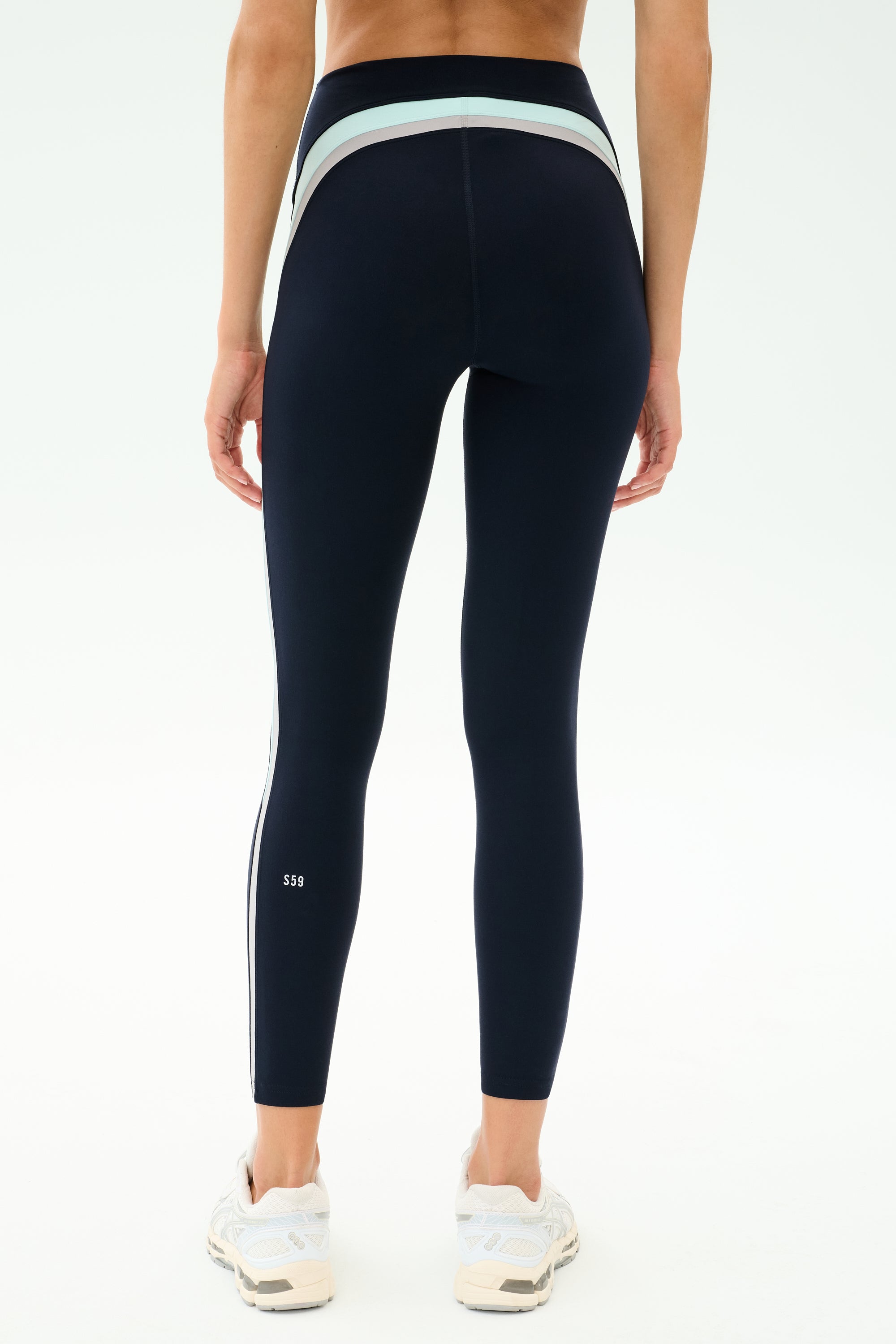 A person is shown from the back in SPLITS59 Emerson Airweight High Waist leggings in Indigo/Dove Grey with white sneakers, against a plain background—ideal attire for Pilates or hot yoga sessions.