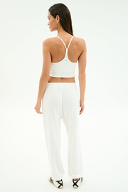 A woman faces away, wearing SPLITS59's Andie Oversized Fleece Varsity 59 Sweatpant in White/59 with a white sports bra and black-striped slide sandals, perfect for cool weather workouts, set against a plain white background.