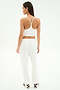 A woman faces away, wearing the SPLITS59 Airweight Crop - White styled as a cropped tank, with loose white pants and striped slide sandals against a plain white background.