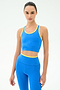 A person stands against a plain background wearing the SPLITS59 Amber Airweight Bralette in Classic Blue/Ray, featuring a cropped scoop-neck design and yellow trim, ideal for hot yoga and crafted from Airweight performance fabric.