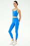 A person wearing the SPLITS59 Amber Airweight Bralette in Classic Blue/Ray stands against a plain white background, styled with cropped scoop-neck design and yellow trim, paired with white sneakers.