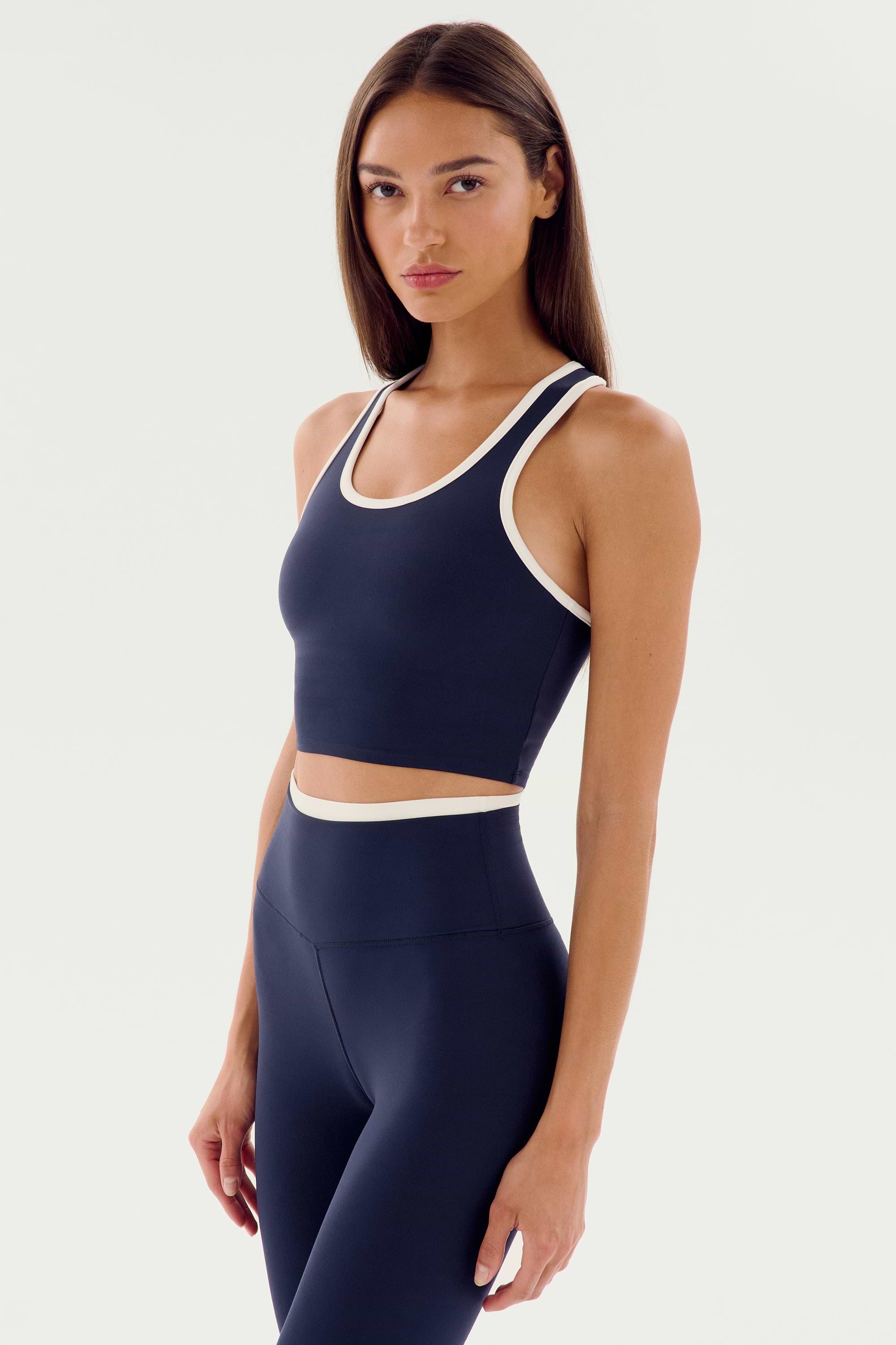 A person stands against a plain background, wearing the SPLITS59 Amber Airweight Bralette - Indigo/White, perfect for a barre or hot yoga session.