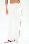 A person wears the SPLITS59 Maxie Rigor Track Pant in White/Indigo with black side stripes and white sneakers with red stripes, standing against a plain light background. Made from soft Rigor fabric for comfort and style.