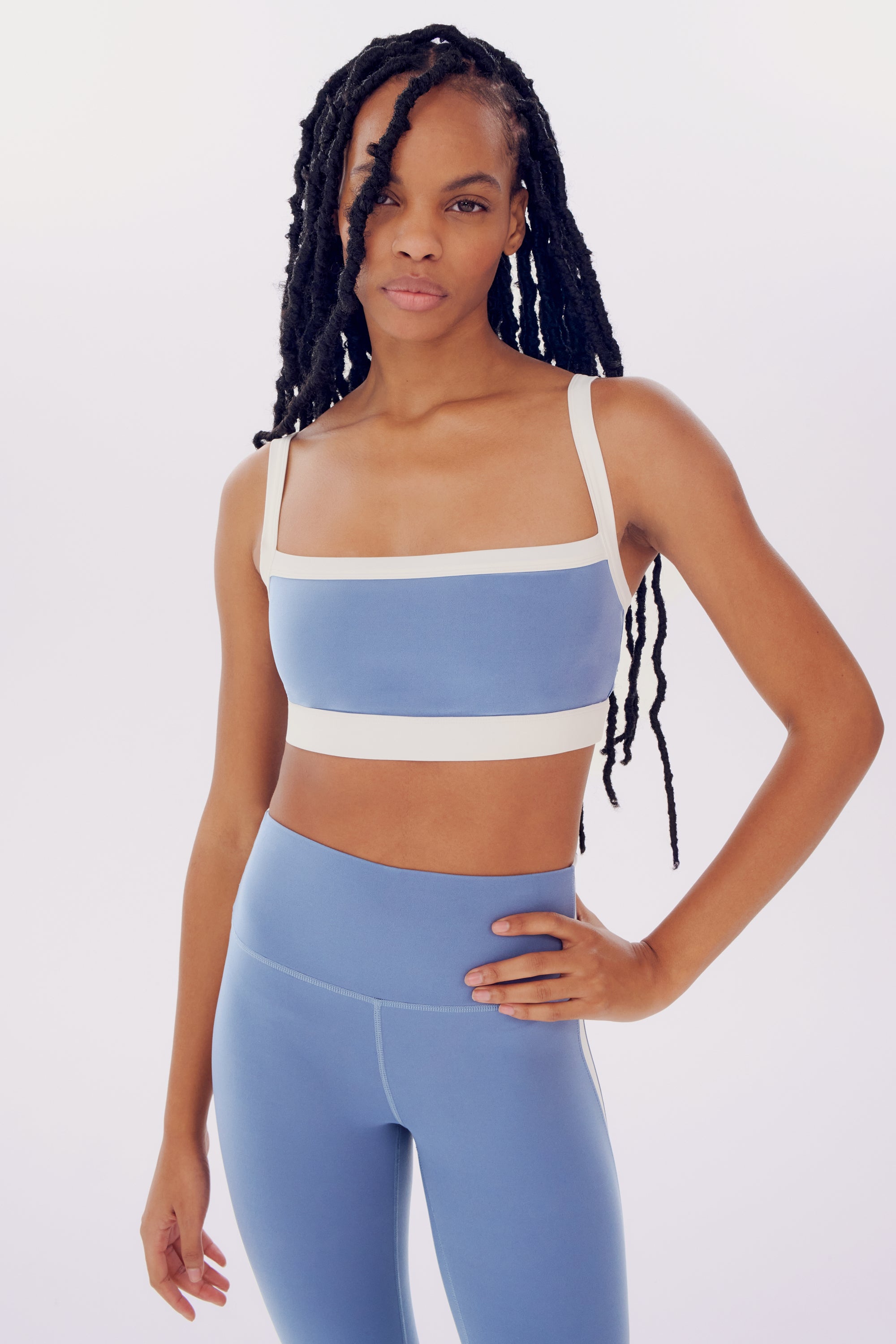 A young woman in a SPLITS59 Monah Rigor Bra - Steel Blue/White and leggings posing confidently against a plain white background.
