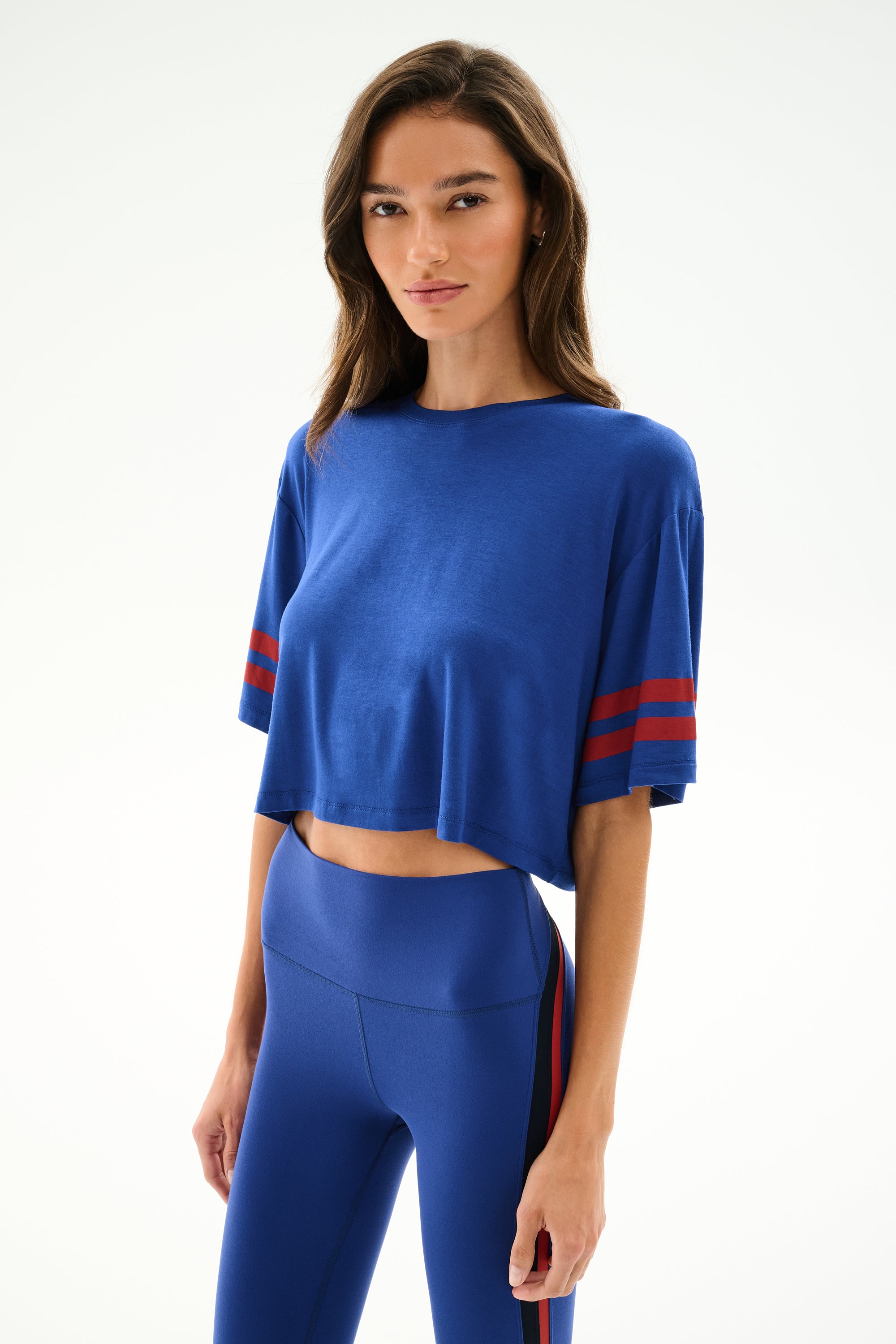 A woman wears the SPLITS59 Djuna Oversized Crop Jersey Tee - Cobalt/Terracotta with matching high-waisted leggings, standing against a plain light background.