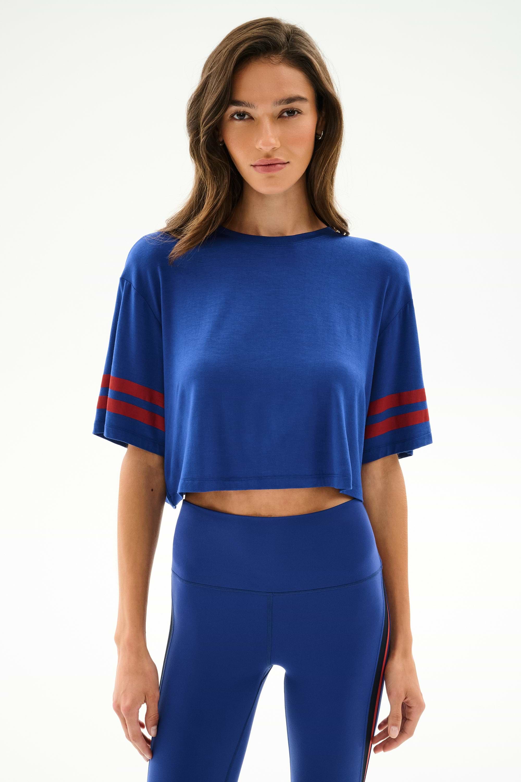 A woman wears the SPLITS59 Djuna Oversized Crop Jersey Tee - Cobalt/Terracotta, paired with matching high-waisted leggings, against a plain white background.