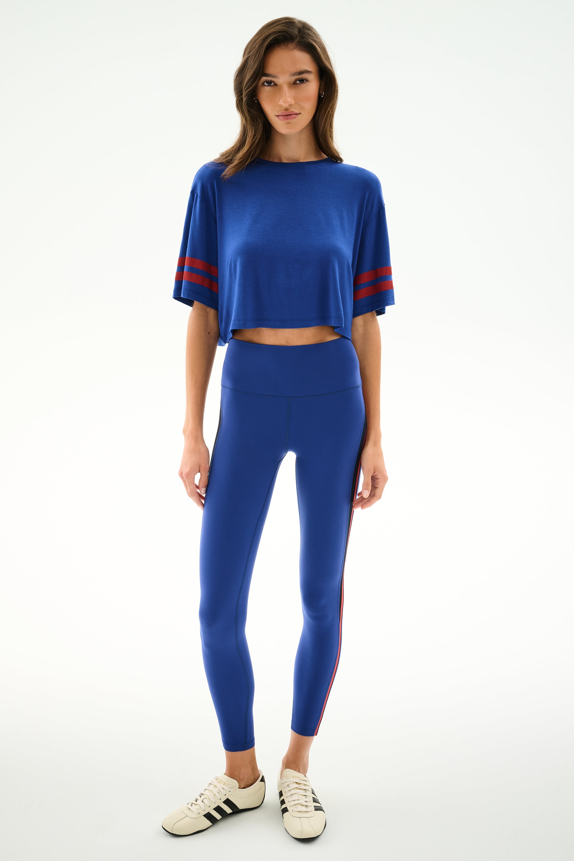 Woman against a white background wears the Djuna Oversized Crop Jersey Tee - Cobalt/Terracotta by SPLITS59, paired with matching leggings and white sneakers with black stripes.