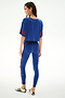 Woman facing away in SPLITS59 Djuna Oversized Crop Jersey Tee - Cobalt/Terracotta and blue leggings, with white sneakers, on a plain white background.