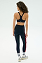 A woman stands facing away, wearing the SPLITS59 Ella Airweight Bra in Indigo/Pirate Red with matching leggings, white socks, and sneakers against a plain light background.