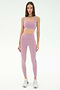 A woman poses in a studio wearing SPLITS59 Margot Rigor Leggings in Blush/Military and a matching light purple sports bra, paired with white athletic shoes.