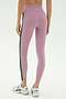 A person wearing SPLITS59 Margot Rigor Legging in mauve with a dark green side stripe and white New Balance sneakers, shown from the back against a plain background.