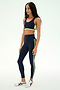 A woman is wearing the SPLITS59 Maci Airweight Bra in Indigo/Limeade, featuring neon yellow-green accents and crafted from a stretchy nylon spandex fabric, paired with white sneakers against a plain light background.