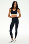 A woman wears the SPLITS59 Maci Airweight Bra in Indigo/Limeade, paired with matching activewear leggings, both crafted from stretchy nylon-spandex fabric. She completes the look with white sneakers and stands against a white background.