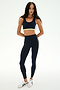 A woman wears the SPLITS59 Maci Airweight Bra in Indigo/Limeade, paired with matching activewear leggings, both crafted from stretchy nylon-spandex fabric. She completes the look with white sneakers and stands against a white background.