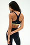 A woman stands facing away, wearing the SPLITS59 Maci Airweight Bra in Indigo/Limeade, paired with matching leggings, both crafted from stretchy nylon spandex activewear, against a plain white background.