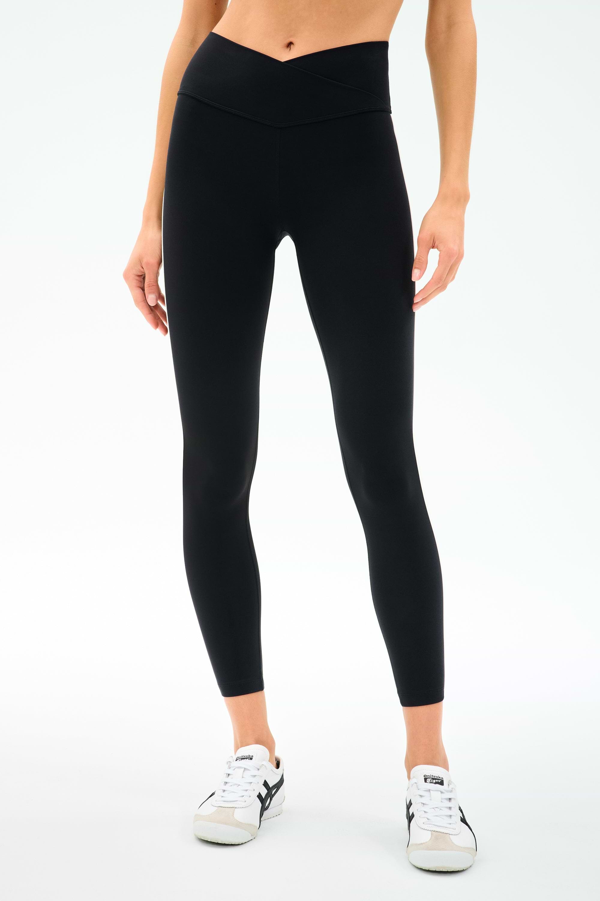 A person wearing SPLITS59 Mia Rigor Legging w/ Stripe in Black/White and white sneakers stands against a plain white background.
