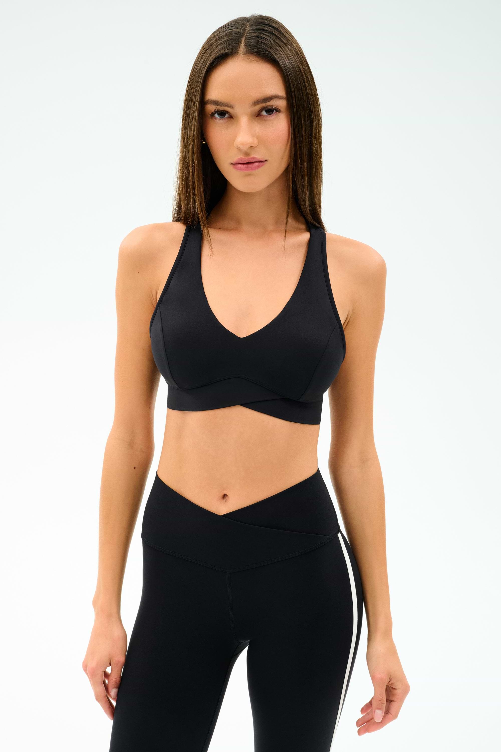 A woman wears the SPLITS59 Mia Rigor Bra in black with high-waisted black leggings, standing against a plain white background—perfect for gym workouts and multi-sport performance.