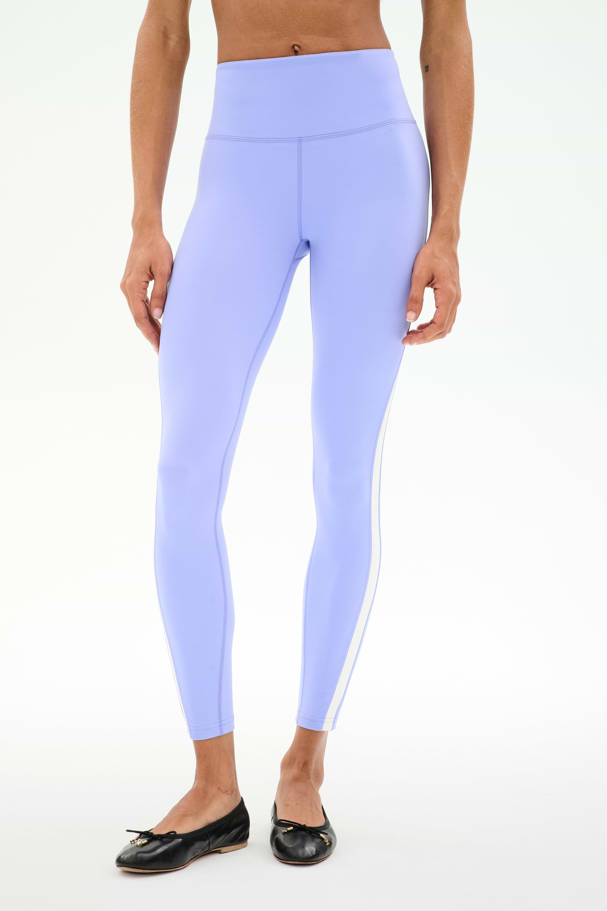 A person wears SPLITS59 Miles High Waist Rigor 7/8 leggings in Purple Haze/White with black ballet flats, standing against a plain white background.