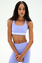 A woman wears the SPLITS59 Miles Rigor Bra in Purple Haze/White with matching leggings, standing against a plain, light background.