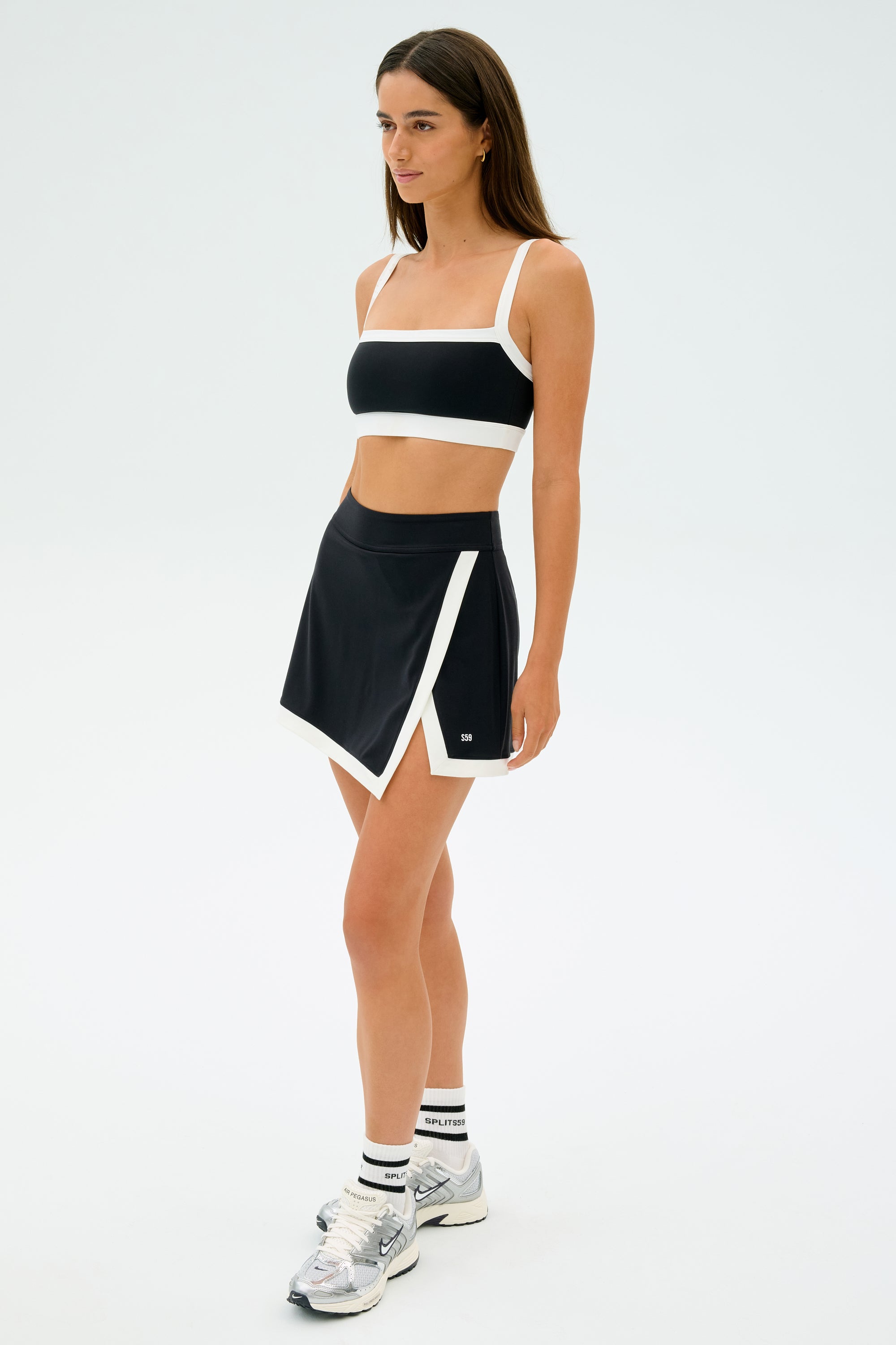 Wearing a chic black and white athletic set, including SPLITS59's Monah Rigor Bra - Black/White for ultimate support, a person poses confidently against a plain backdrop.