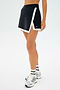 Someone wearing the SPLITS59 Monah Rigor Skort in black/white with matching socks and silver running shoes stands against a plain background.
