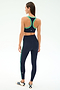 A woman stands on a white background wearing the SPLITS59 Robbie Airweight Bra in Indigo/Spearmint, paired with matching leggings and white sneakers with navy stripes.