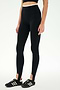 A person is wearing the SPLITS59 River Dual Waist Airweight Stirrup leggings in Black/Creme, paired with a black crop top and black Adidas sneakers, standing against a plain white background.