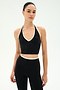A woman models the SPLITS59 Rory Airweight Halter Bralette in Black/Creme, featuring white trim, paired with high-waisted leggings—all crafted from a sleek nylon-spandex blend—standing against a plain white background.