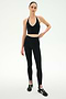 A woman stands against a plain background, wearing the SPLITS59 Rory Airweight Halter Bralette in Black/Creme, paired with high-waisted black leggings and black athletic shoes.