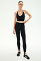 A woman stands against a plain background, wearing the SPLITS59 Rory Airweight Halter Bralette in Black/Creme, paired with high-waisted black leggings and black athletic shoes.