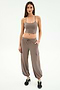 A woman stands against a white background, wearing SPLITS59's Nico Airweight Cargo Pant in Lentil with pockets, styled like joggers, a taupe crop top, and black sneakers.