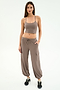 A woman stands against a white background, wearing SPLITS59's Nico Airweight Cargo Pant in Lentil with pockets, styled like joggers, a taupe crop top, and black sneakers.