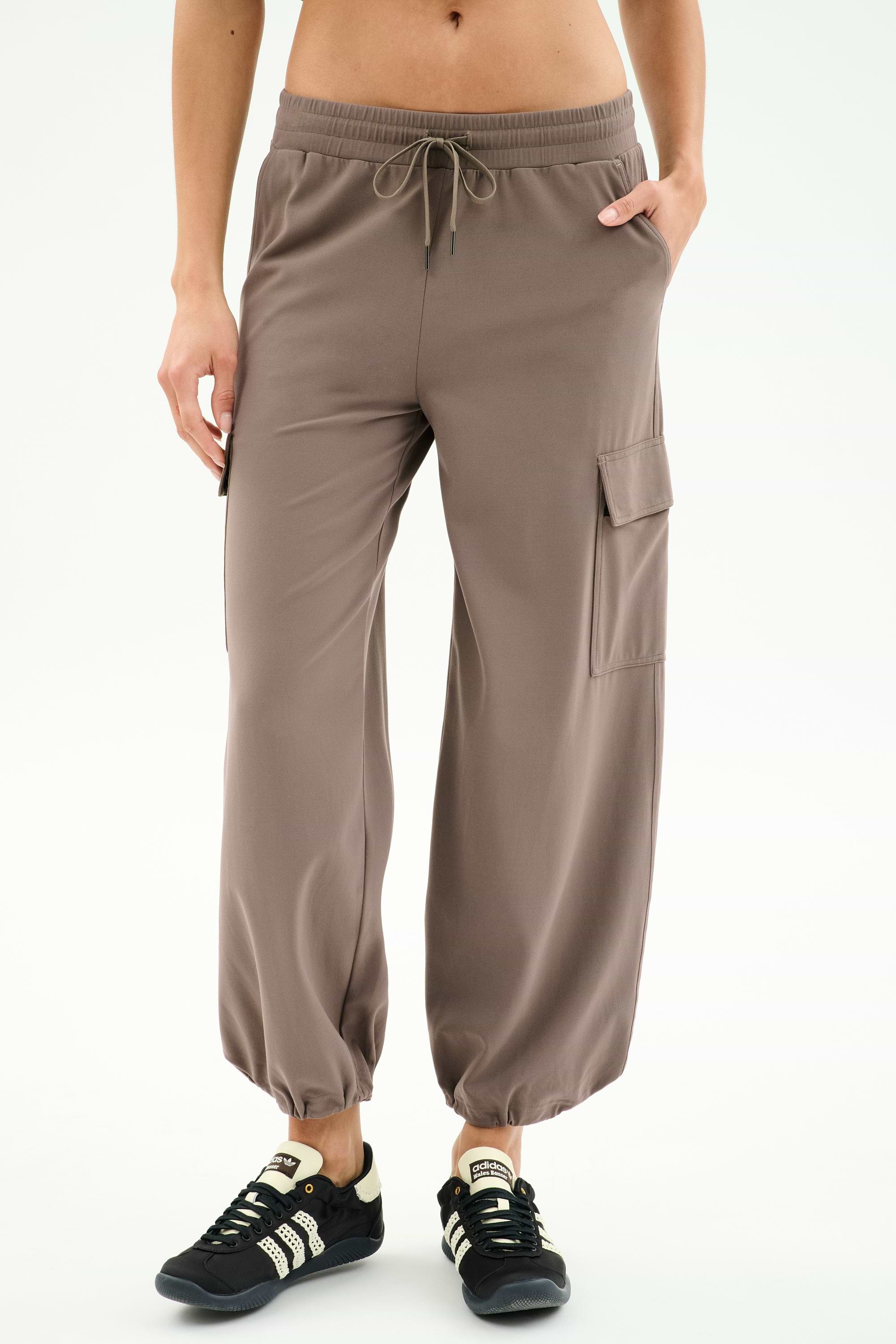 Wearing SPLITS59 Nico Airweight Cargo Pant in Lentil with side pockets and drawstring waist, paired with black sneakers—ideal for lightweight comfort during workouts, shown against a white background.