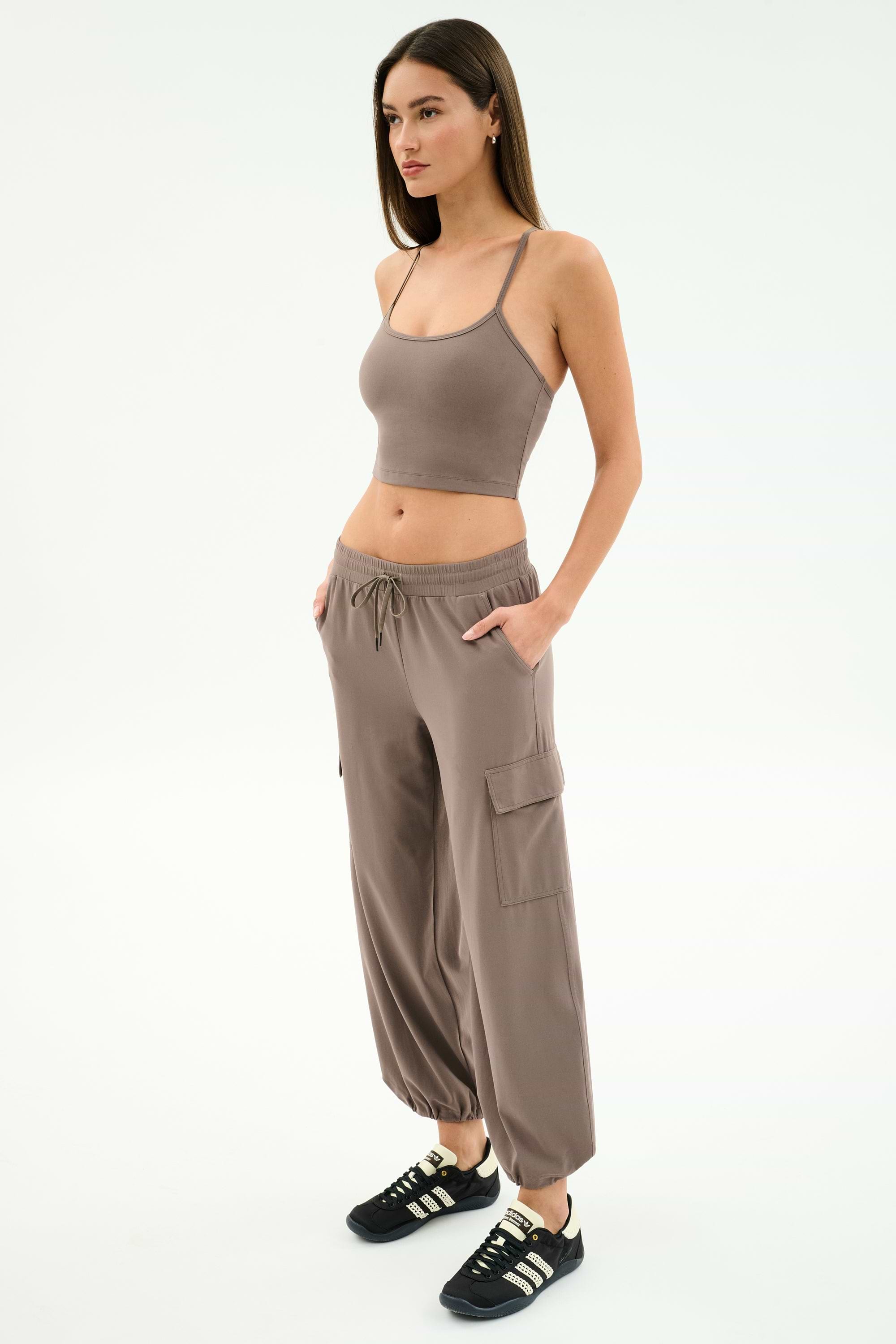 A woman stands in a studio, hands in pockets, wearing SPLITS59’s Nico Airweight Cargo Pant in Lentil with a taupe crop top and black sneakers, perfect for lightweight comfort, facing slightly to the right.