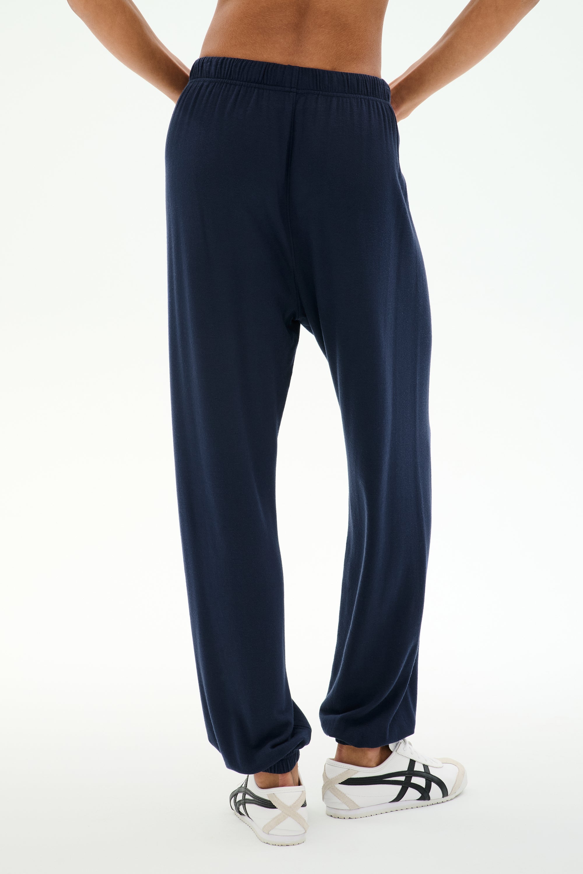 A person wearing the SPLITS59 Andie Oversized Fleece Sweatpant in Indigo and white sneakers stands with their back to the camera against a white background, ready for cool weather workouts in this comfy Los Angeles-made style.
