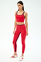 A woman wears the SPLITS59 Easton Rigor High Waist 7/8 in Pirate Red/Indigo, featuring compressive fabric, along with white and red sneakers, standing against a plain light background.
