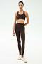 A person stands against a plain background wearing SPLITS59's River High Waist Airweight Stirrup leggings in Dark Chocolate, paired with a matching sports bra and white sneakers.