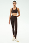 A person stands against a plain background wearing SPLITS59's River High Waist Airweight Stirrup leggings in Dark Chocolate, paired with a matching sports bra and white sneakers.