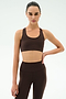 A woman poses against a plain background in SPLITS59’s Sara Airweight Bra - Dark Chocolate and matching leggings, one hand on her hip and a neutral expression—ideal for hot yoga or Pilates.
